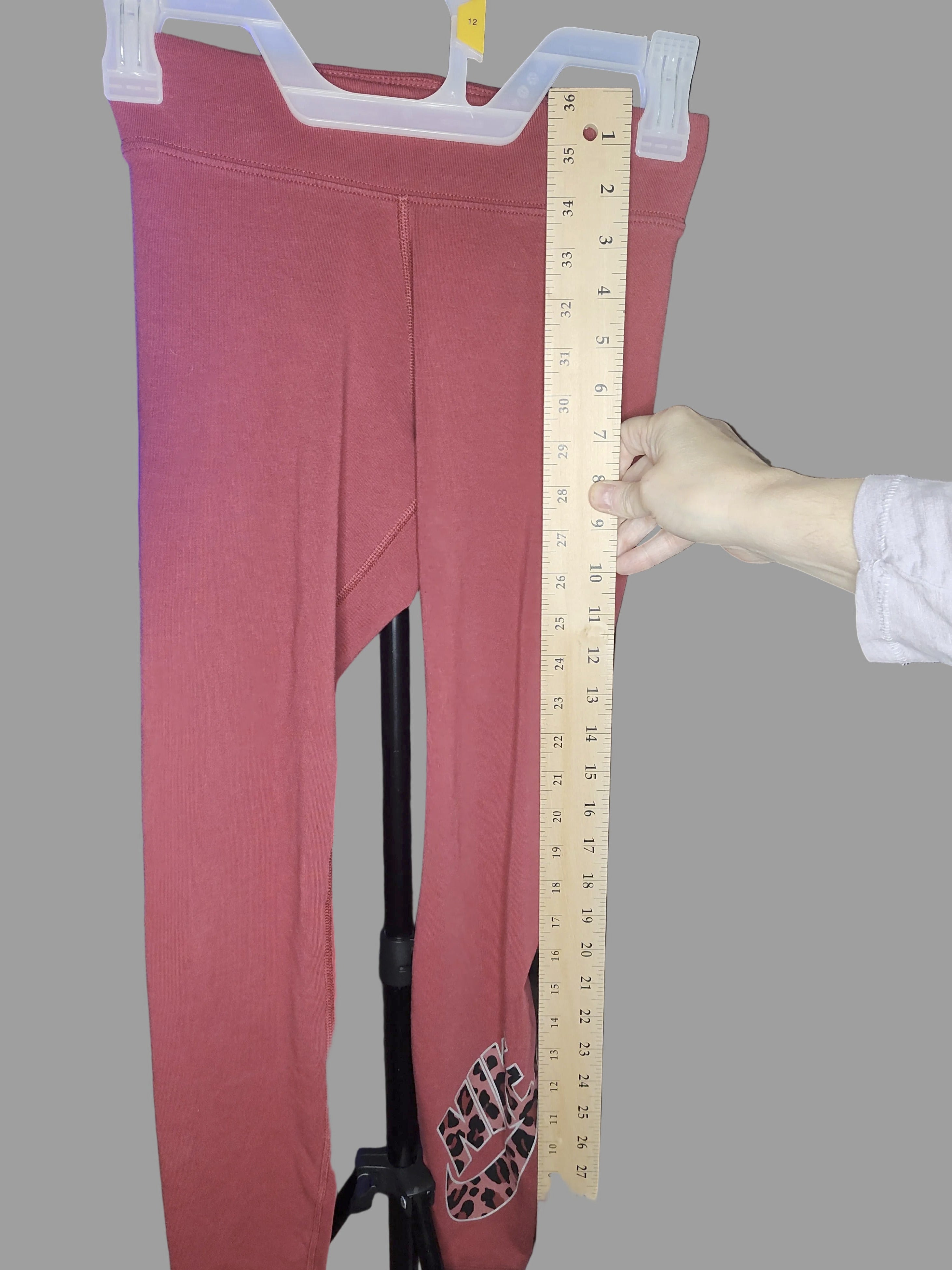 Red pants on a hanger with a ruler for size measurement against a gray background