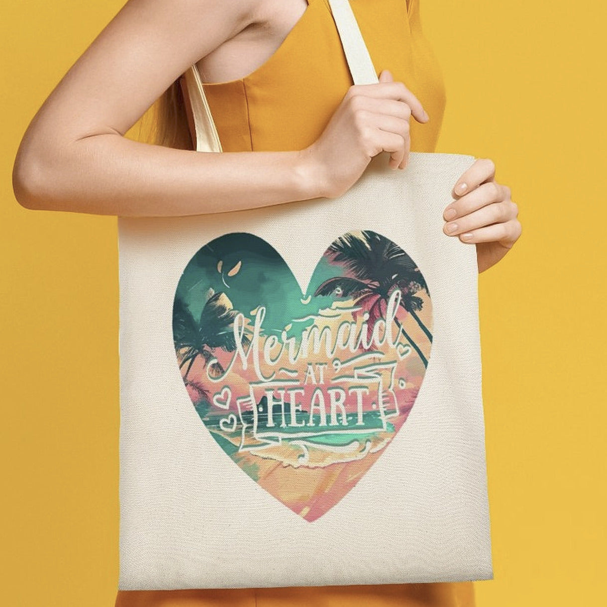 Person holding a tote bag with a heart design and 'Mermaid at Heart' text on a yellow background